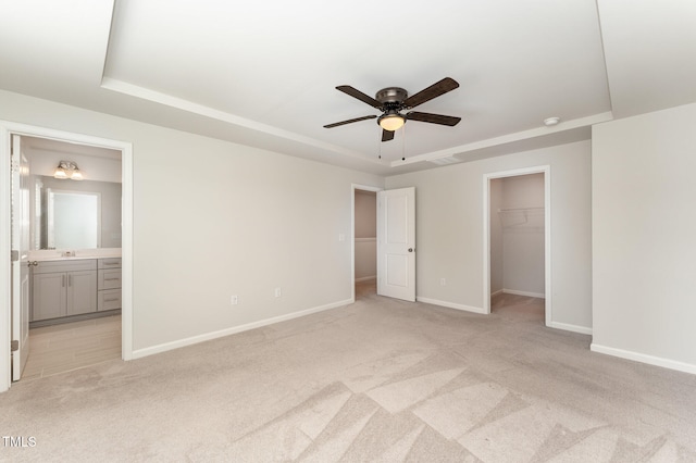 unfurnished bedroom with ceiling fan, a raised ceiling, connected bathroom, and a walk in closet