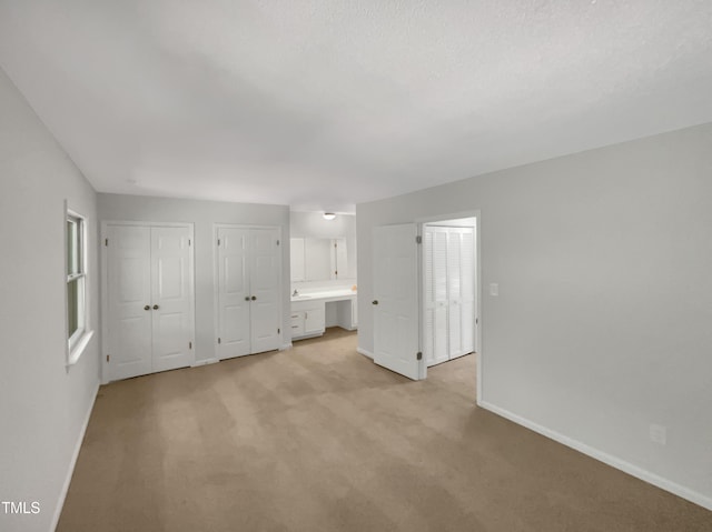 unfurnished bedroom featuring two closets and light carpet