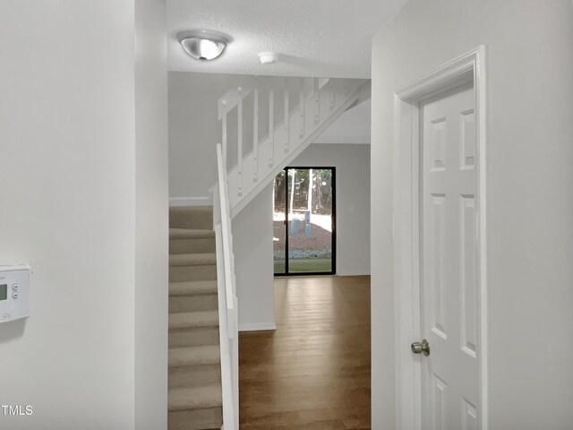 corridor with a textured ceiling and hardwood / wood-style floors