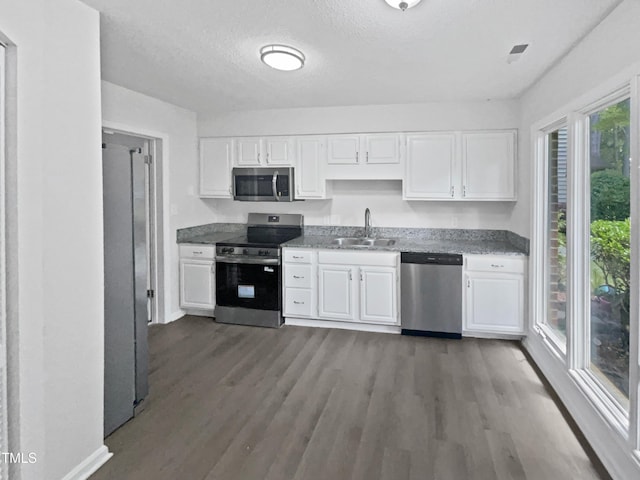 kitchen with baseboards, a sink, wood finished floors, stainless steel appliances, and white cabinets