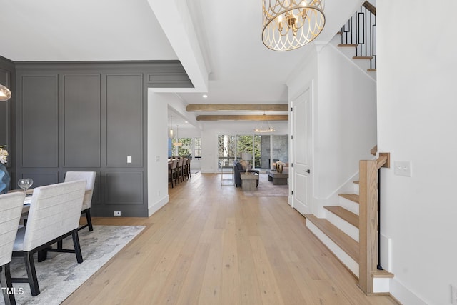 entrance foyer featuring a chandelier, a decorative wall, stairs, light wood-type flooring, and beamed ceiling