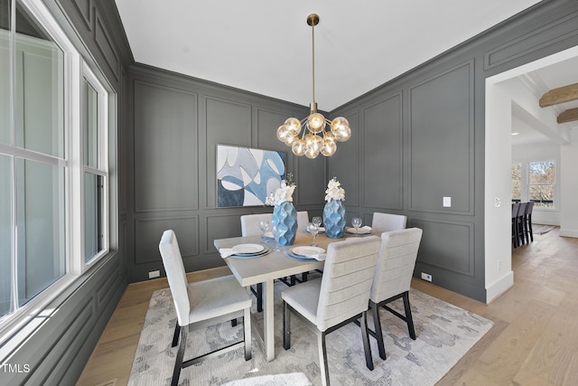 dining area with light wood-style floors, a chandelier, crown molding, and a decorative wall