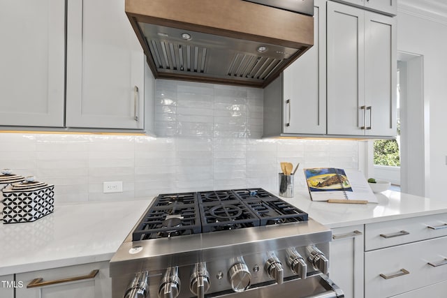 kitchen with stainless steel range with gas cooktop, light stone countertops, backsplash, and exhaust hood