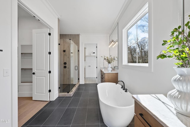 bathroom with a walk in closet, crown molding, a freestanding bath, a stall shower, and vanity