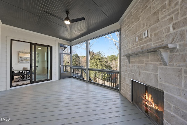 unfurnished sunroom with a ceiling fan and an outdoor stone fireplace