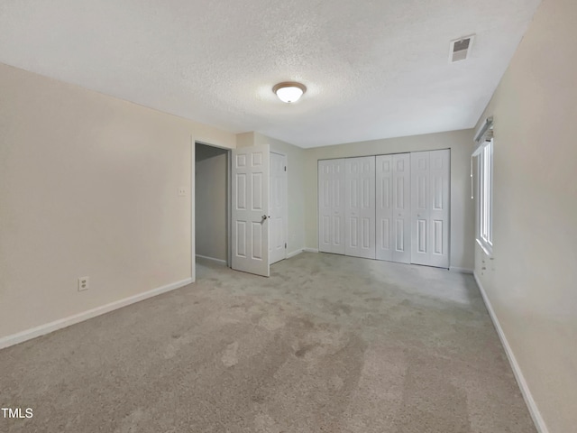 unfurnished bedroom with a textured ceiling, light carpet, and a closet