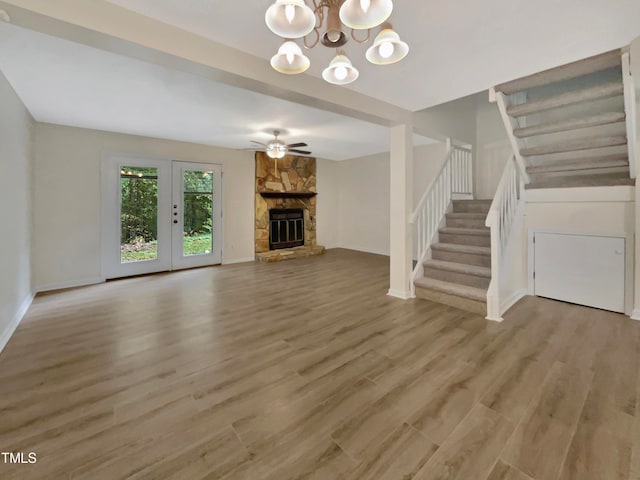 unfurnished living room with a stone fireplace, ceiling fan with notable chandelier, and light hardwood / wood-style floors