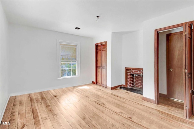 unfurnished bedroom with light wood-type flooring, a brick fireplace, and a closet