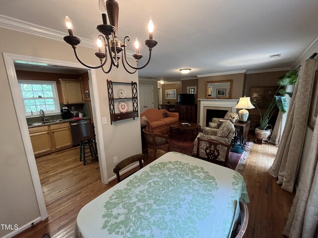 dining space featuring sink, crown molding, an inviting chandelier, and hardwood / wood-style flooring