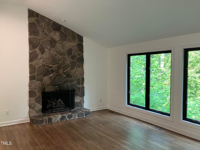 unfurnished living room featuring dark wood-type flooring, vaulted ceiling, and a stone fireplace