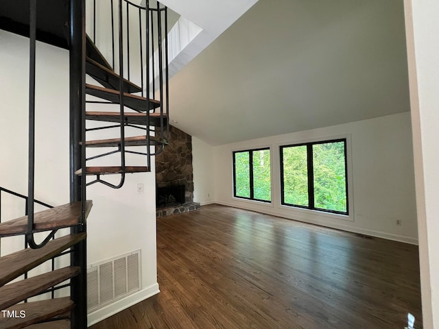 staircase featuring a stone fireplace, hardwood / wood-style floors, and high vaulted ceiling