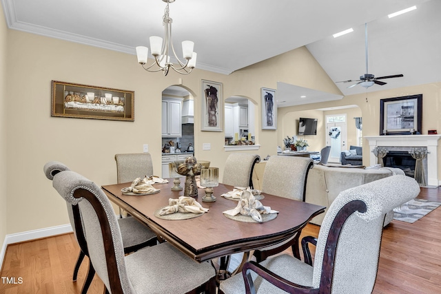 dining space with arched walkways, crown molding, a fireplace, and light wood-style floors