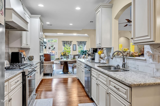 kitchen with appliances with stainless steel finishes, a sink, light stone counters, and wood finished floors