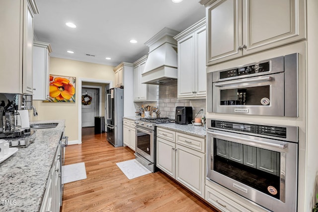 kitchen featuring custom range hood, high quality appliances, a sink, light stone countertops, and backsplash