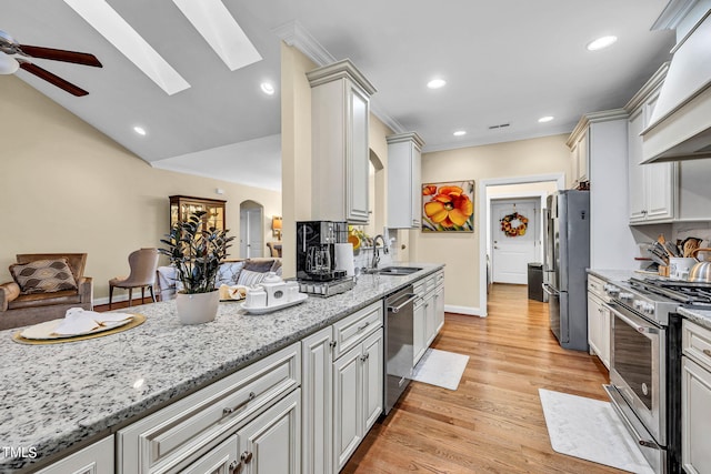 kitchen featuring arched walkways, a sink, open floor plan, appliances with stainless steel finishes, and light stone countertops