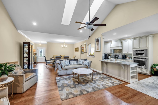 living area with light wood finished floors, a skylight, ornamental molding, and ceiling fan with notable chandelier