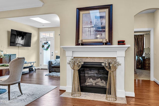 living room featuring a fireplace with flush hearth, baseboards, arched walkways, and wood finished floors