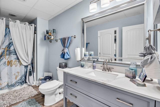 bathroom with curtained shower, toilet, a paneled ceiling, wood finished floors, and vanity