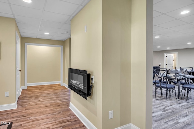 hallway featuring a paneled ceiling, recessed lighting, light wood-style flooring, and baseboards