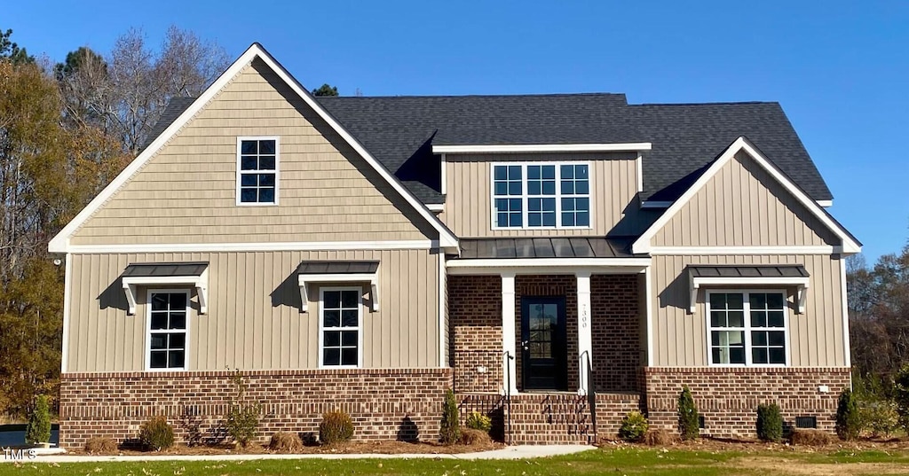 view of front of house featuring metal roof, roof with shingles, brick siding, and a standing seam roof