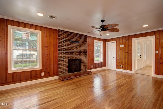 unfurnished living room with crown molding, plenty of natural light, a fireplace, and light hardwood / wood-style floors