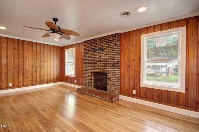 unfurnished living room with ceiling fan, wooden walls, a fireplace, ornamental molding, and light hardwood / wood-style floors