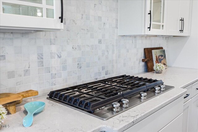 kitchen featuring stainless steel gas stovetop, light stone counters, decorative backsplash, and white cabinetry