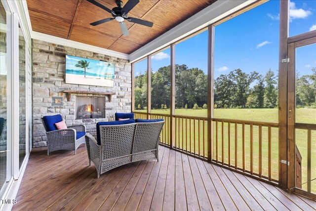 sunroom with an outdoor stone fireplace, a healthy amount of sunlight, ceiling fan, and wooden ceiling