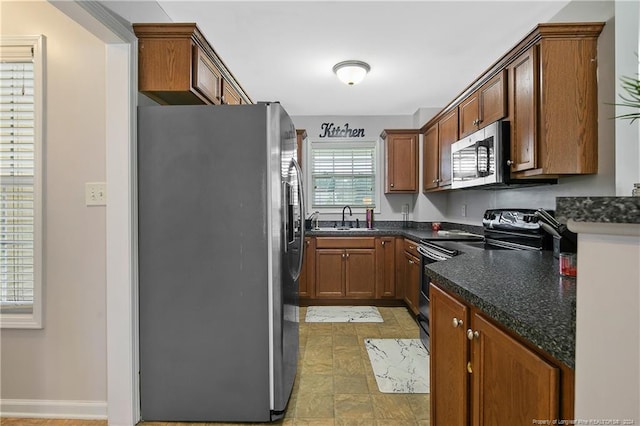 kitchen with appliances with stainless steel finishes, dark stone countertops, and sink