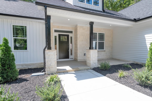 doorway to property with a porch, stone siding, roof with shingles, and board and batten siding