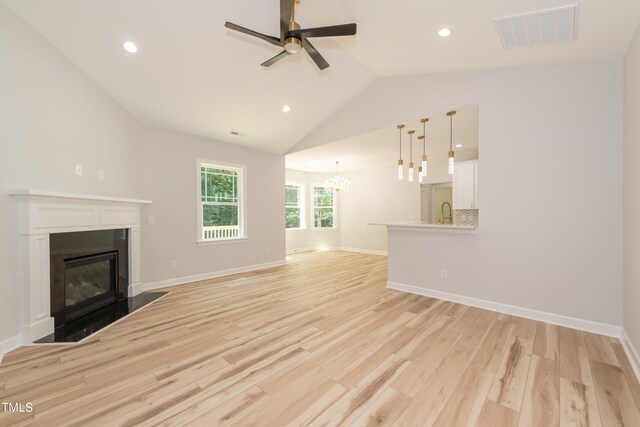 unfurnished living room with sink, high vaulted ceiling, light hardwood / wood-style floors, and ceiling fan with notable chandelier