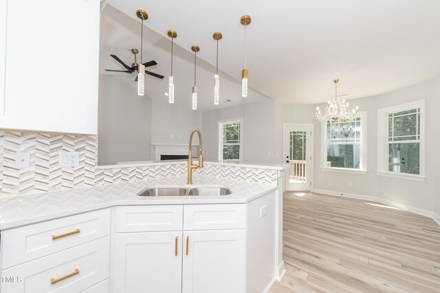 kitchen with backsplash, decorative light fixtures, sink, light wood-type flooring, and ceiling fan with notable chandelier