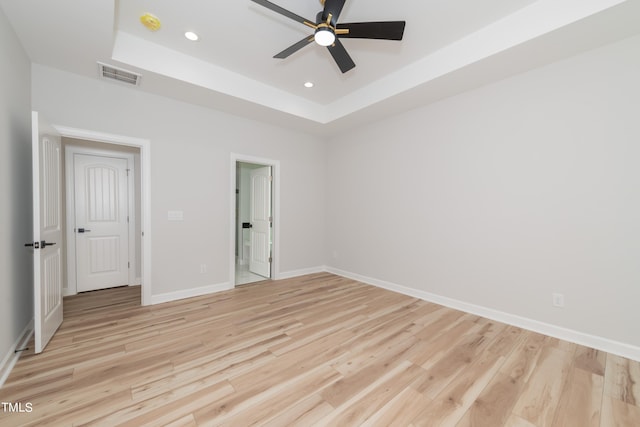 unfurnished bedroom with ceiling fan, light wood-type flooring, and a raised ceiling