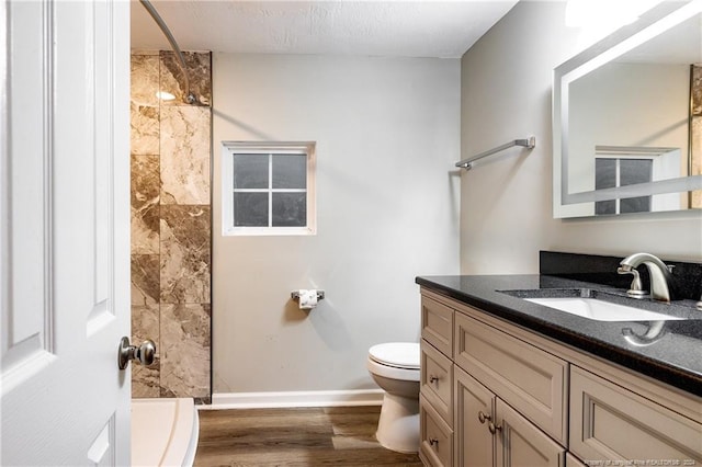 bathroom with tiled shower, vanity, toilet, and wood-type flooring