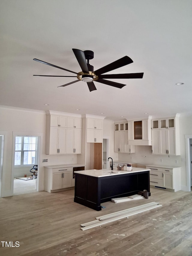 kitchen with a kitchen island with sink, ornamental molding, white cabinets, light wood finished floors, and light countertops