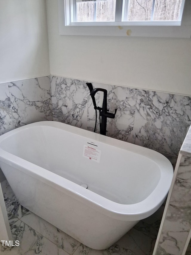 full bath with marble finish floor and a freestanding tub