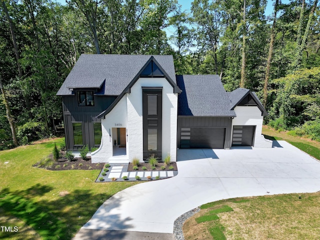 view of front of property with a front lawn, board and batten siding, an attached garage, driveway, and roof with shingles