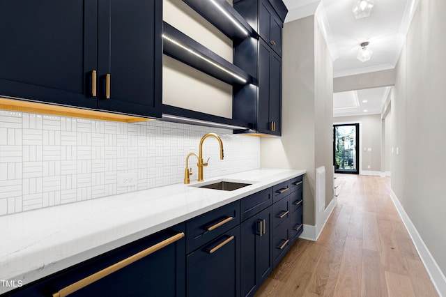 kitchen with backsplash, ornamental molding, sink, blue cabinetry, and light hardwood / wood-style floors