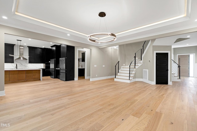 unfurnished living room with sink, light wood-type flooring, and a raised ceiling