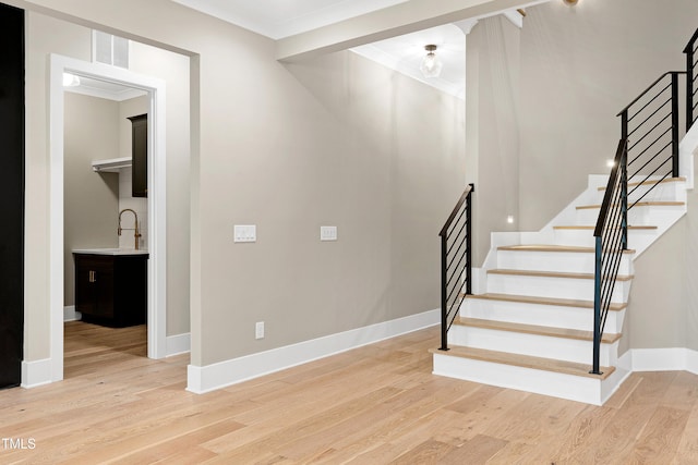 stairway with sink, crown molding, and wood-type flooring