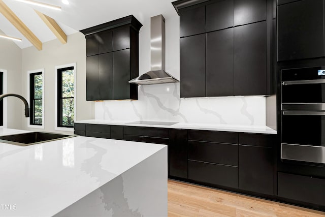 kitchen featuring decorative backsplash, vaulted ceiling with beams, wall chimney range hood, sink, and light hardwood / wood-style floors