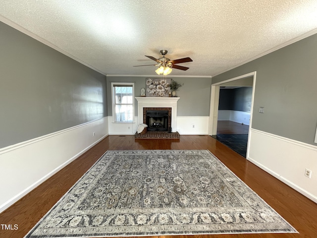 living room featuring crown molding, ceiling fan, a fireplace, a textured ceiling, and dark hardwood / wood-style flooring