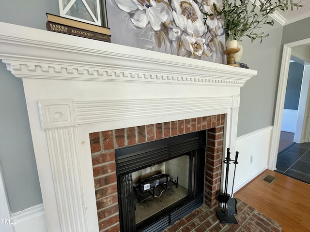 interior details featuring ornamental molding, wood-type flooring, and a brick fireplace