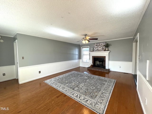 unfurnished living room with dark wood-type flooring, a brick fireplace, a textured ceiling, ornamental molding, and ceiling fan