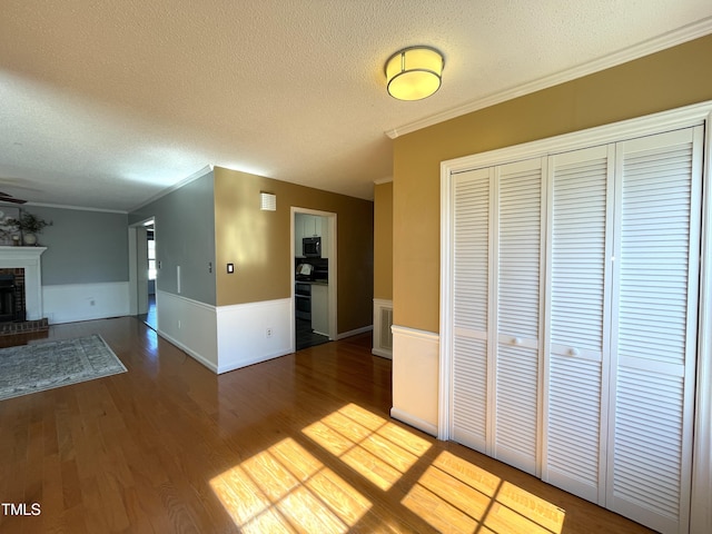 unfurnished living room with wood-type flooring, a brick fireplace, ornamental molding, and a textured ceiling