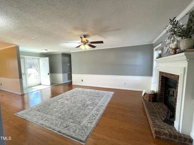 living room featuring ornamental molding, ceiling fan, a brick fireplace, dark wood-type flooring, and a textured ceiling