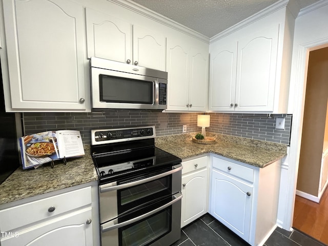 kitchen with white cabinetry, ornamental molding, stainless steel appliances, and dark stone counters