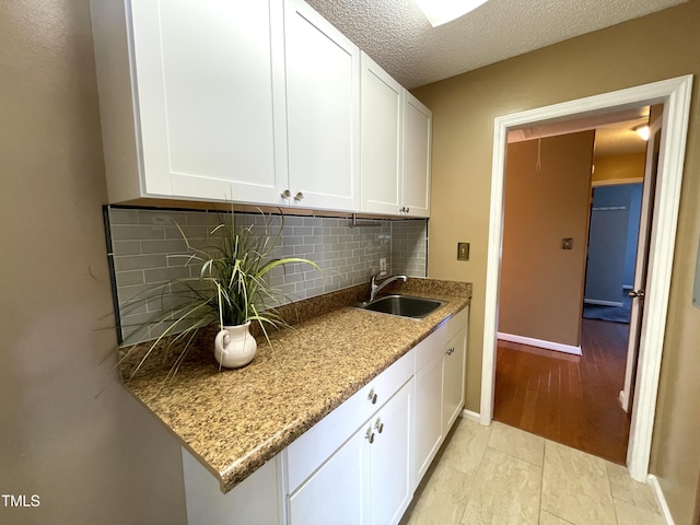 kitchen with sink, white cabinetry, light stone counters, a textured ceiling, and backsplash