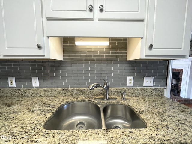 kitchen with tasteful backsplash, sink, white cabinetry, and light stone countertops