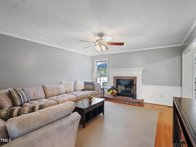 living room featuring a ceiling fan, a textured ceiling, light wood-style floors, a fireplace, and crown molding